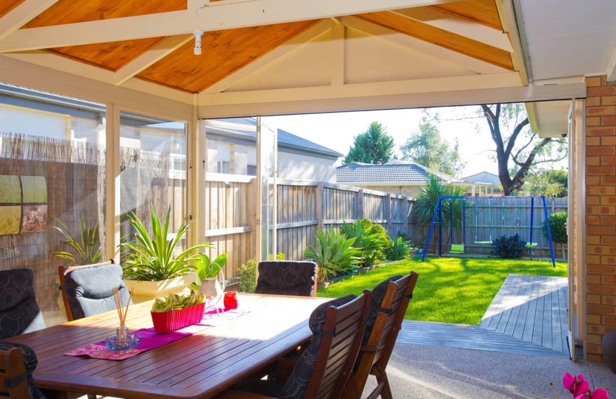 Alfresco dining room enclosed with Accolade PVC weather screens, opening onto a landscaped backyard