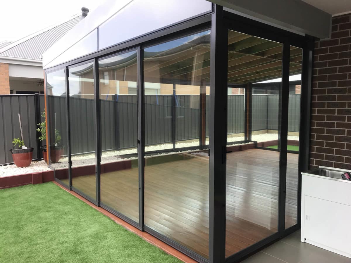 Modern glass and aluminium framed weather screen enclosure along a home's alfresco deck